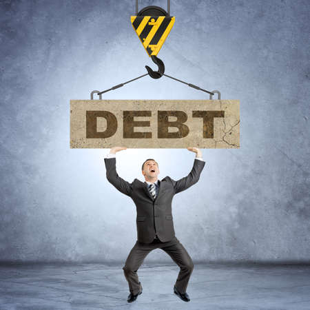 Businessman holding heavy word debt on grey wall backgroundの写真素材