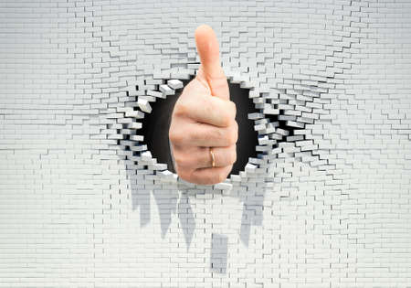 Businessmans hand showing ok through hole in brick wallの写真素材