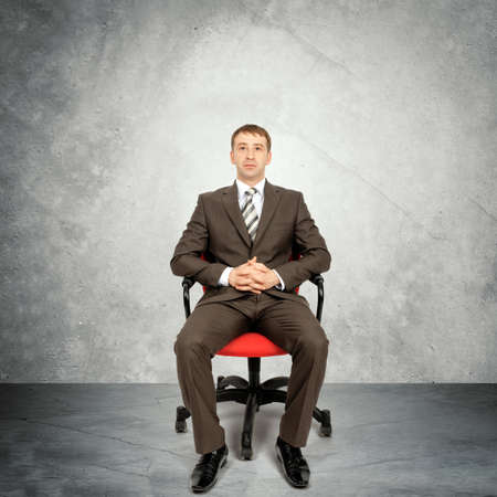 Businessman sitting in chair on grey wall background, business conceptの写真素材