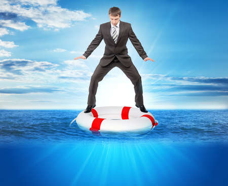 Buisnessman on lifebuoy looking down in sea, balance conceptの写真素材