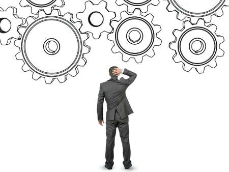 Confused businessman in front of cog wheels isolated on white backgroundの写真素材