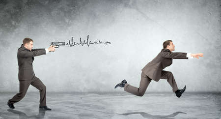 Businessman shooting  another man on grey wall backgroundの写真素材