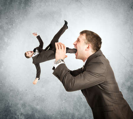 Businessman eating little man on grey wall backgroundの写真素材
