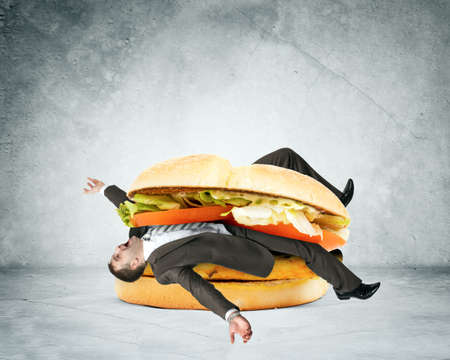 Businessman inside hamburger on grey wall backgroundの写真素材