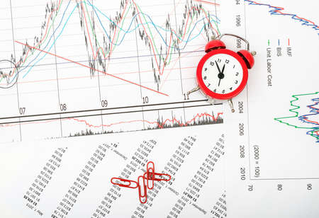 Alarm clock with paper clips on grpahical charts background, business concept