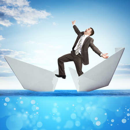 Businessman in broken paper boat in blue sea, business conceptの写真素材