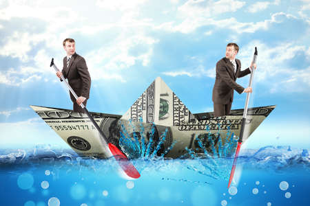 Two businessmen in dollar boat rowing in different ways in blue sea, business conceptの写真素材