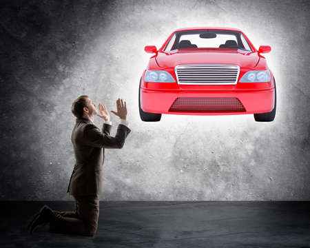 Businessman on knees in front of car on grey wall backgroundの写真素材