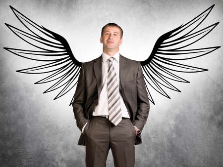 Businessman with drawn angel wings looking at camera on grey background