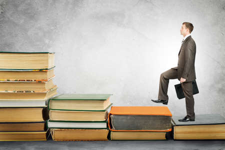 Businessman with portfolio goes up stairs of books. Education conceptの写真素材