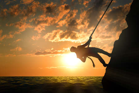 Business man climbs mountain within help of rope, sunsetの写真素材