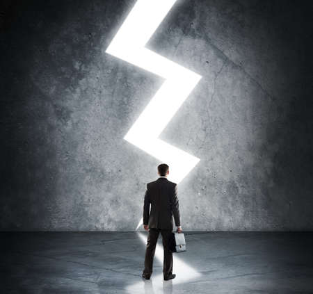 Businessman with briefcase standing in light of lightning signの写真素材