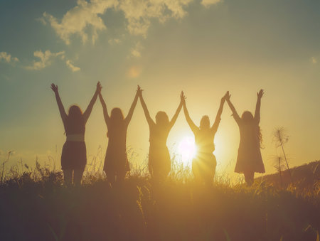 Joyful silhouetted figures raising their hands against a warm sunset sky, conveying togetherness and celebration.の素材