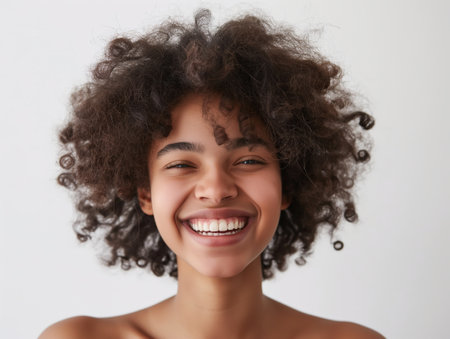 Close-up of a smiling young woman with curly hair against a white background, radiating happiness and confidence.の素材