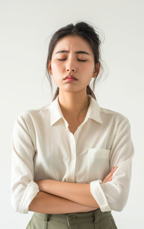 A young Asian woman with closed eyes, expressing frustration or stress, crossing her arms against a white background.の素材