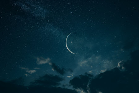 A serene night sky featuring a slender crescent moon among stars with subtle clouds.