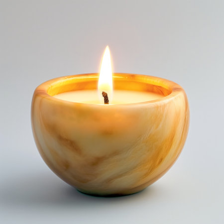 A single lit candle with a warm glow in a smooth, marbled container on a light background.の素材