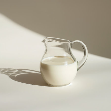 A glass milk jug filled with milk, casting a shadow on a light surface under natural sunlight.の素材