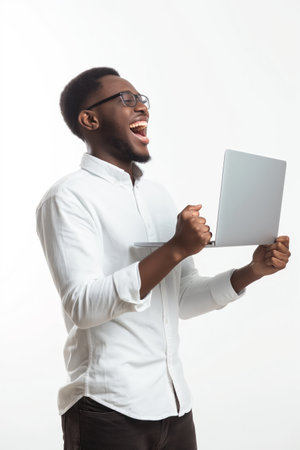 Young man in white shirt, celebrating success with laptop in hand on white background.の素材