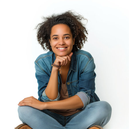 A happy young woman in denim attire seated with crossed legs and a cheerful smile.の素材