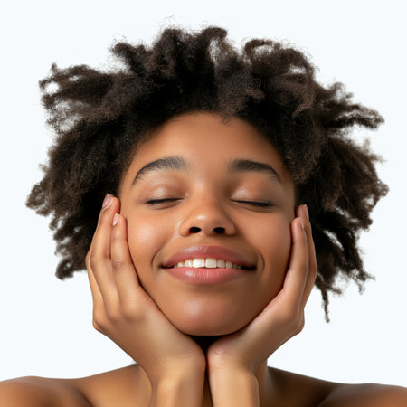 Close-up of a smiling young woman with closed eyes, touching her cheeks, exuding happiness and confidence.の素材