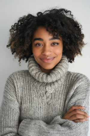A content young woman with curly hair and a warm sweater exudes comfort and ease.の素材