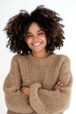 Confident young woman with a bright smile, wearing a cozy sweater, arms crossed.の素材