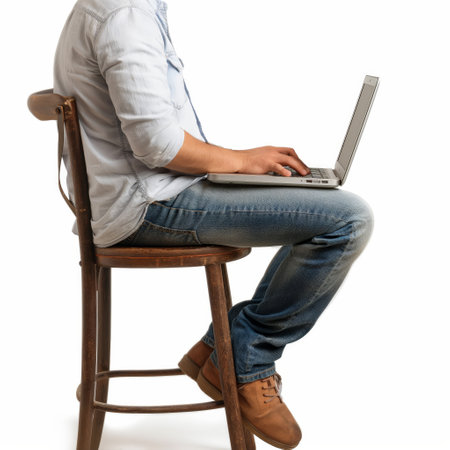 Person seated on a wooden stool using a laptop, exemplifying flexible modern work environmentsの素材