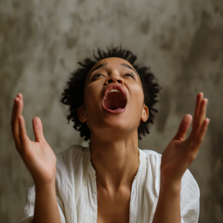 A woman in a white top with an expression of joy and surprise, hands raised, against a textured grey backdrop.の素材