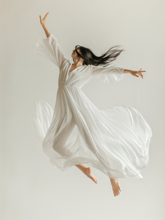 Woman in flowing white dress captured mid-leap against a pale background, embodying freedom and grace.の素材