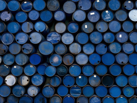 Large collection of stacked blue industrial oil barrels with various signs of wear and markings.の素材
