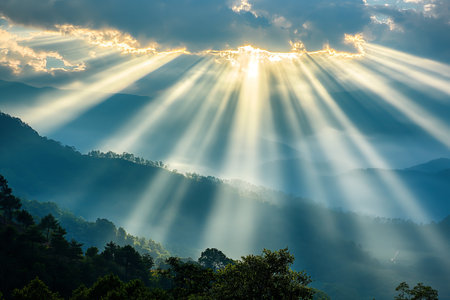 Sunbeams pierce through clouds over misty mountains, creating a dramatic celestial sceneの素材