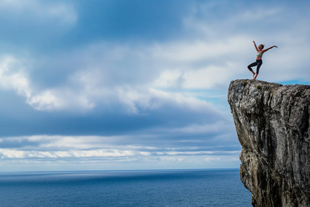 Person standing victoriously on a rock above the sea under a cloudy skyの素材