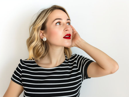 Stylish young woman in striped attire looking thoughtfully upwards.の素材