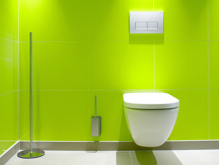 Bright lime green tiled wall with sleek white toilet and metallic toilet brush holder in modern restroom design.の素材