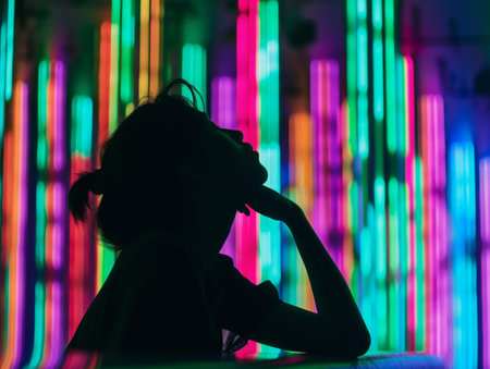 Silhouette of a person deep in thought, with vibrant neon light background creating an atmosphere of contemplation and modernity.の素材