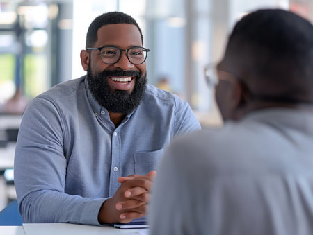 A cheerful man with glasses and a beard smiles during a business meeting in a modern office setting.の素材