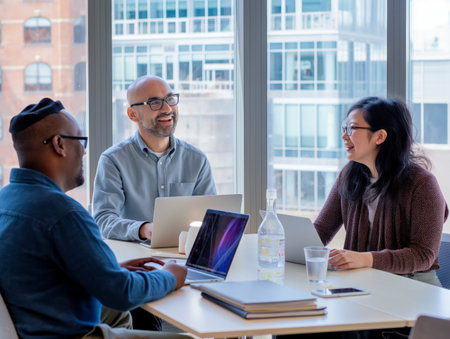 Diverse colleagues engaged in a lively discussion around a table with laptops in a bright office.の素材