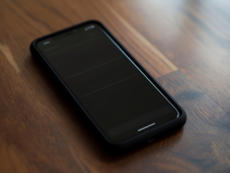 Close-up of a smartphone with a black screen resting on a wooden surface, highlighting modern technology.の素材