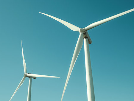 Two large white wind turbines stand tall against a clear blue sky, capturing renewable energy.の素材