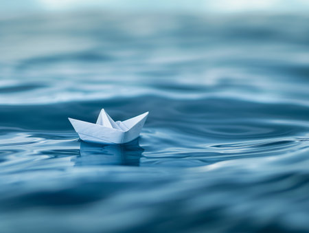 A small white paper boat floats on the calm, rippling blue water, creating a serene and peaceful sceneの素材