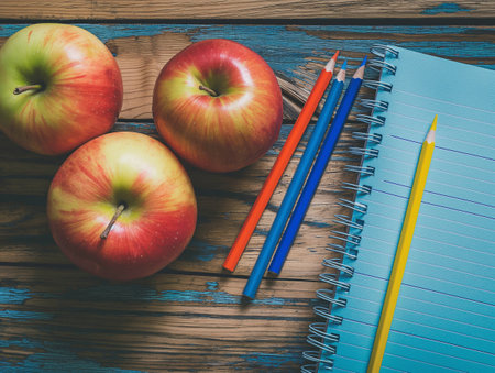 Three apples, colored pencils, and a blue spiral notebook lie on a rustic wooden table with peeling blue paintの素材