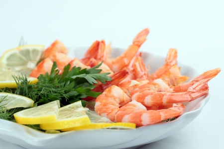 cooked shrimp with fresh herbs and lemon on a plate on a white backgroundの写真素材