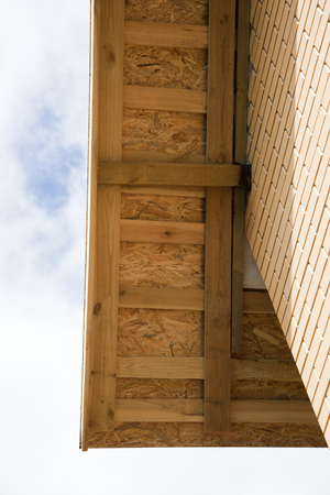 Wall and Roof of the house with exposed wooden beams on the background of blue sky.
