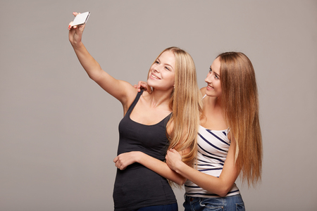 Two friends girls making self portrait with a smartphone, sending kisses, over on a gray backgroundの写真素材