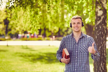 Happy male student with thumbs up holding a notebookの写真素材
