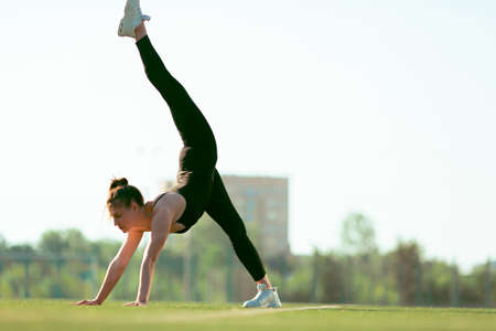 young good looking girl in black sport outfit doing gymnastics handstand in the splits in park