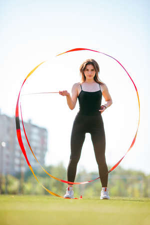 young good looking girl in black sport outfit doing gymnastics in park holding gymnastic stripeの写真素材