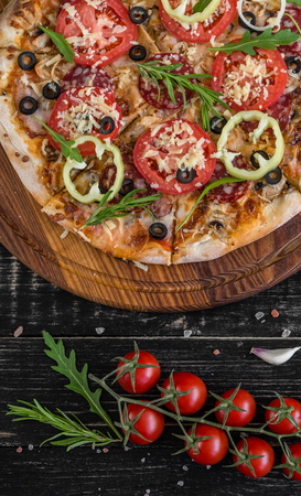 Vegetables, mushrooms and tomatoes pizza on a black wooden background. It can be used as a backgroundの写真素材