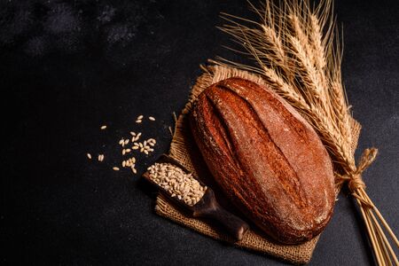Fresh fragrant bread with grains and cones of wheat against a dark backgroundの写真素材